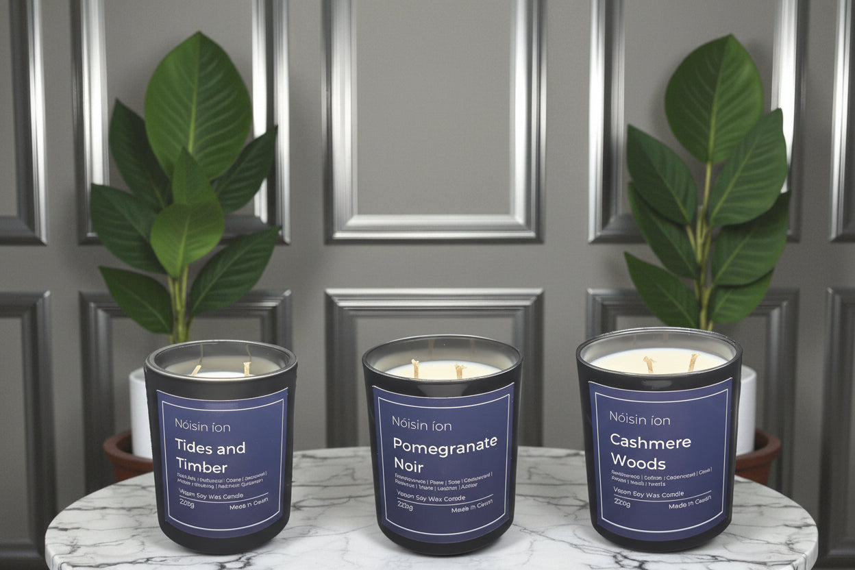 Three candles with labels on a marble surface with plants and decorative balls.