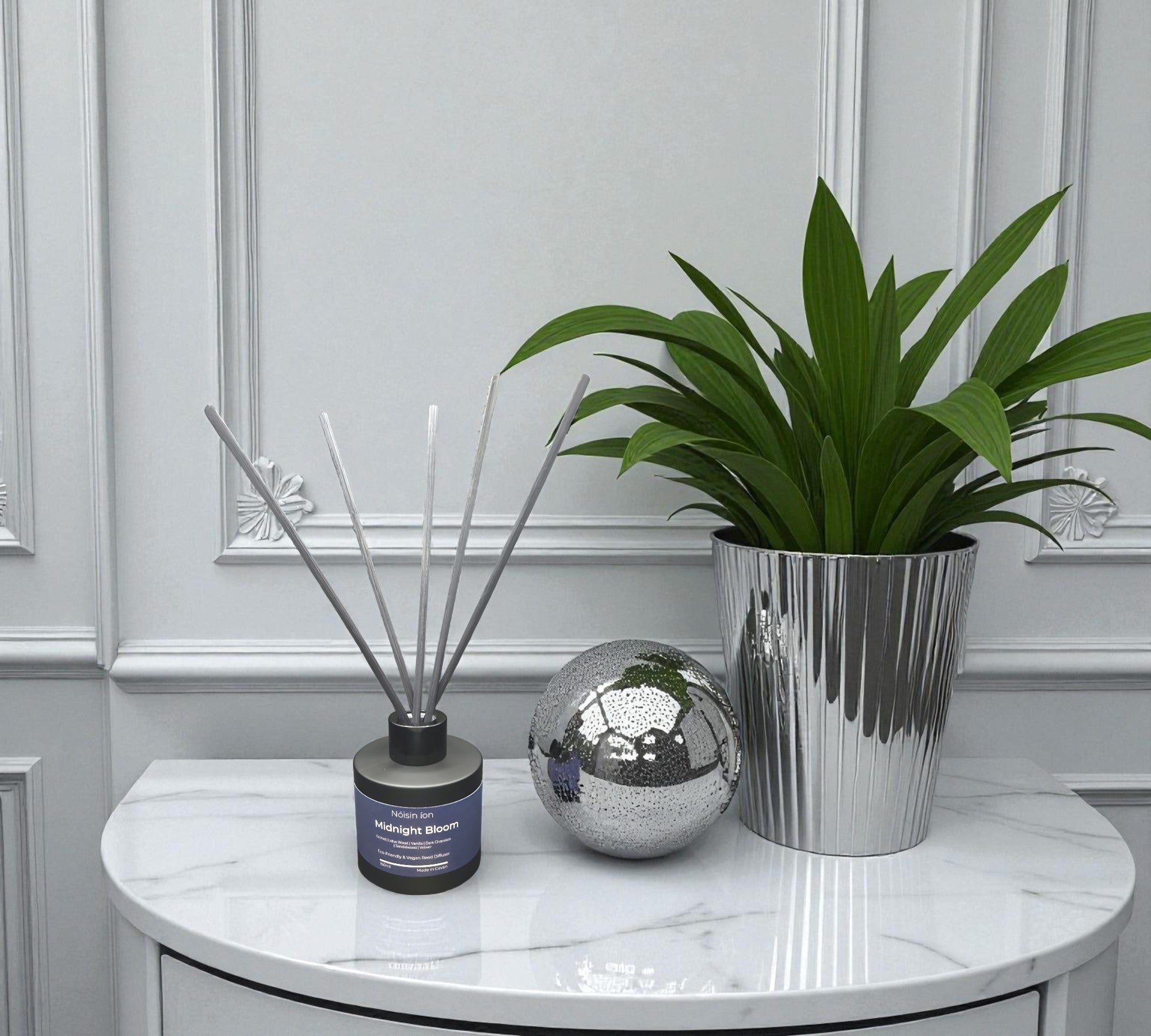Decorative items including a plant, diffuser, and decorative ball on a marble surface.