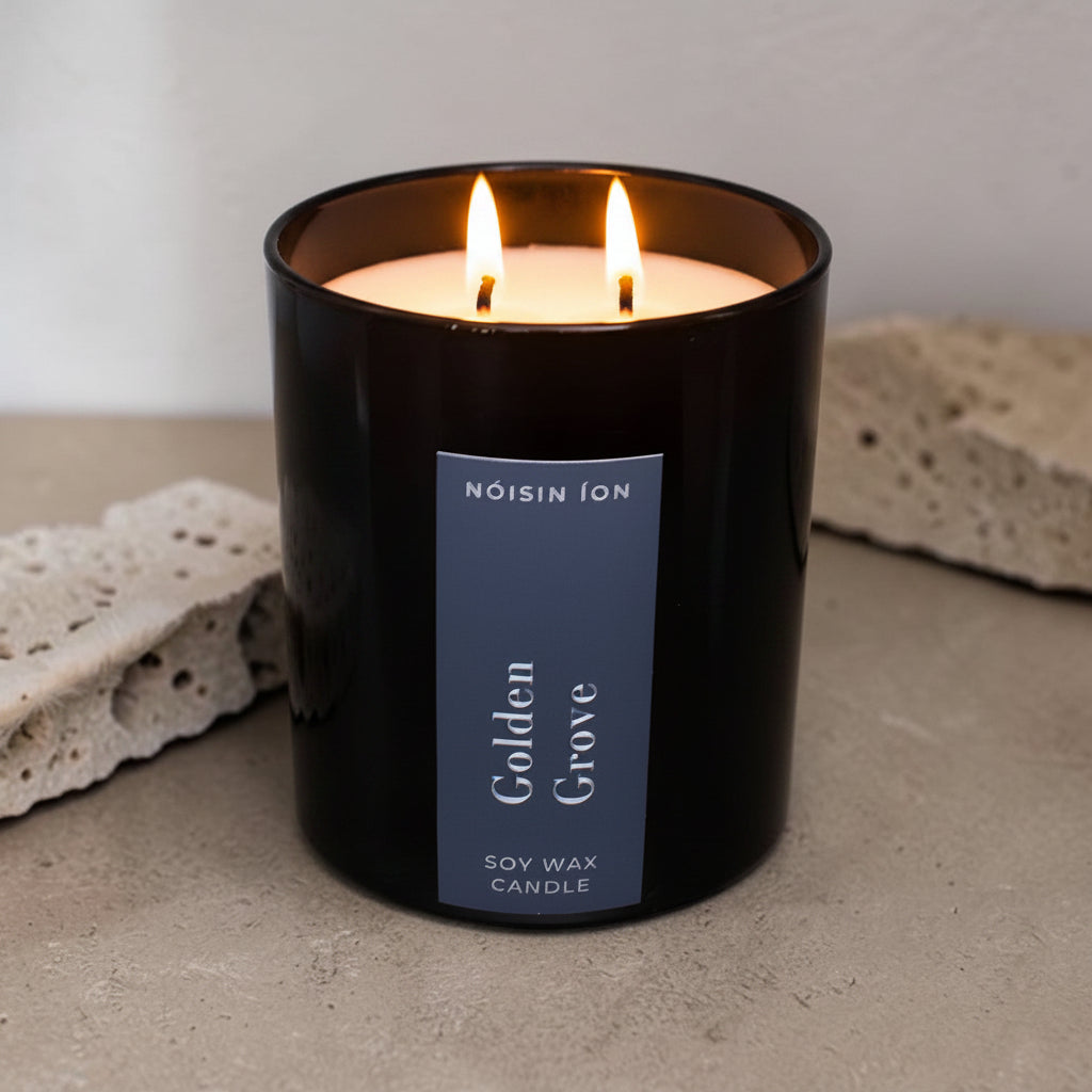 Lit Golden Grove luxury soy wax candle in a black gloss jar with warm citrus and woodland-inspired fragrance by Nóisin Íon.