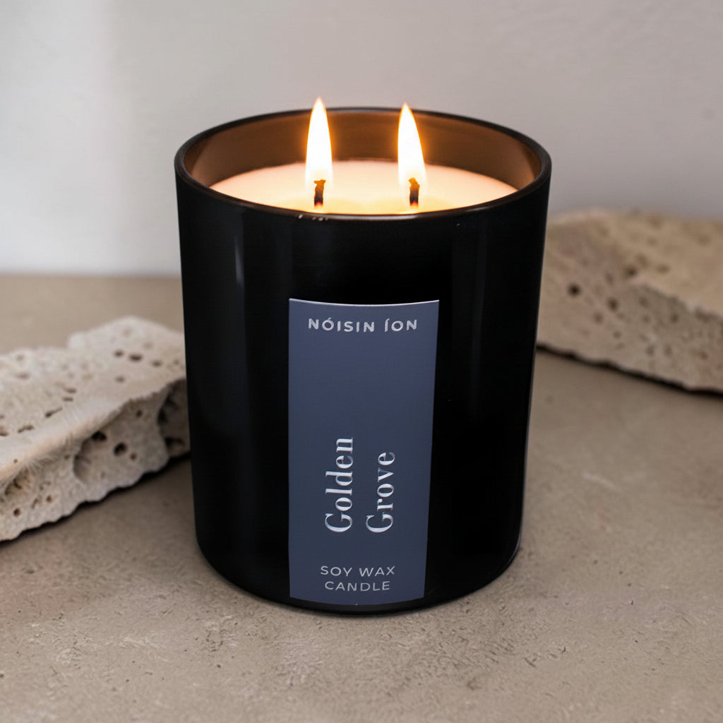 Lit Golden Grove luxury soy wax candle in a black gloss jar with warm citrus and woodland-inspired fragrance by Nóisin Íon.